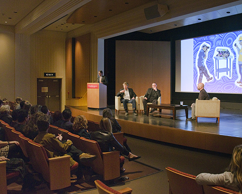 A panel of people sit in chairs on stage