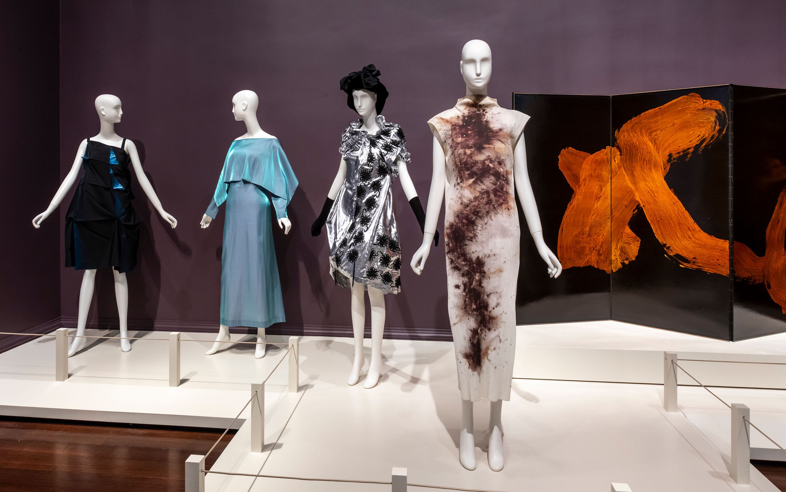 Four ornate dresses and a large black screen with orange brushstroke design