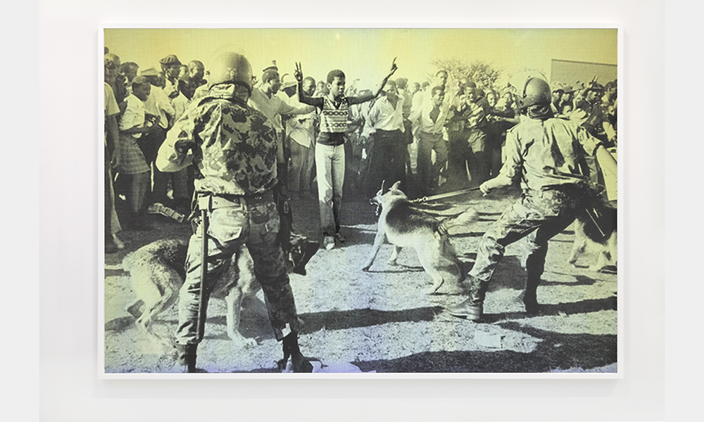 Hank Willis Thomas' Freedom for Soweto, with flash, behind the boy, a large group of other African Americans stand together, in front of the boy, armed men hold back attack dogs lunging for the boy