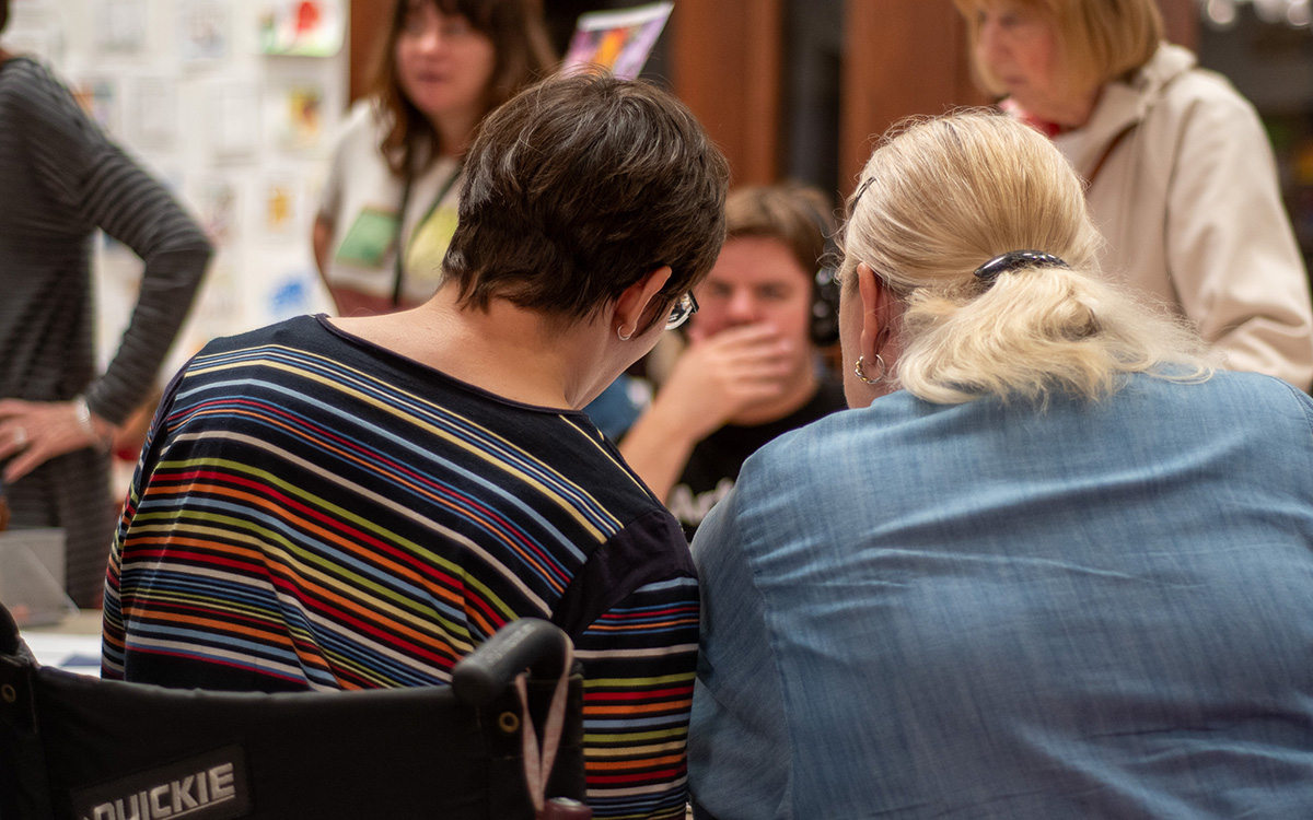 A white person in a wheelchair makes crafts with a friend