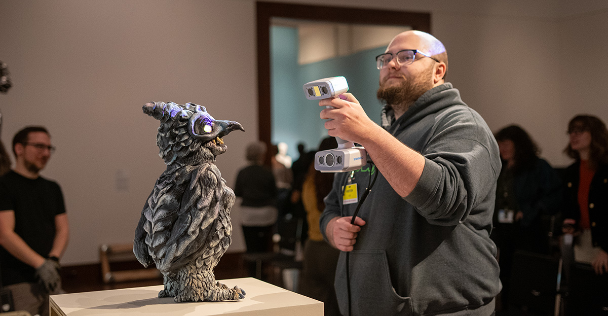 A white man holds an IR scanner and points it at a 3D artwork