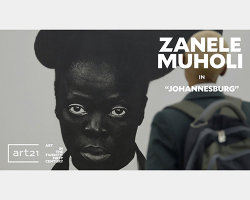 A visitor looks at a massive image of a dark-skinned person, featuring the text "Zanele Muholi in 'Johannesburg'"