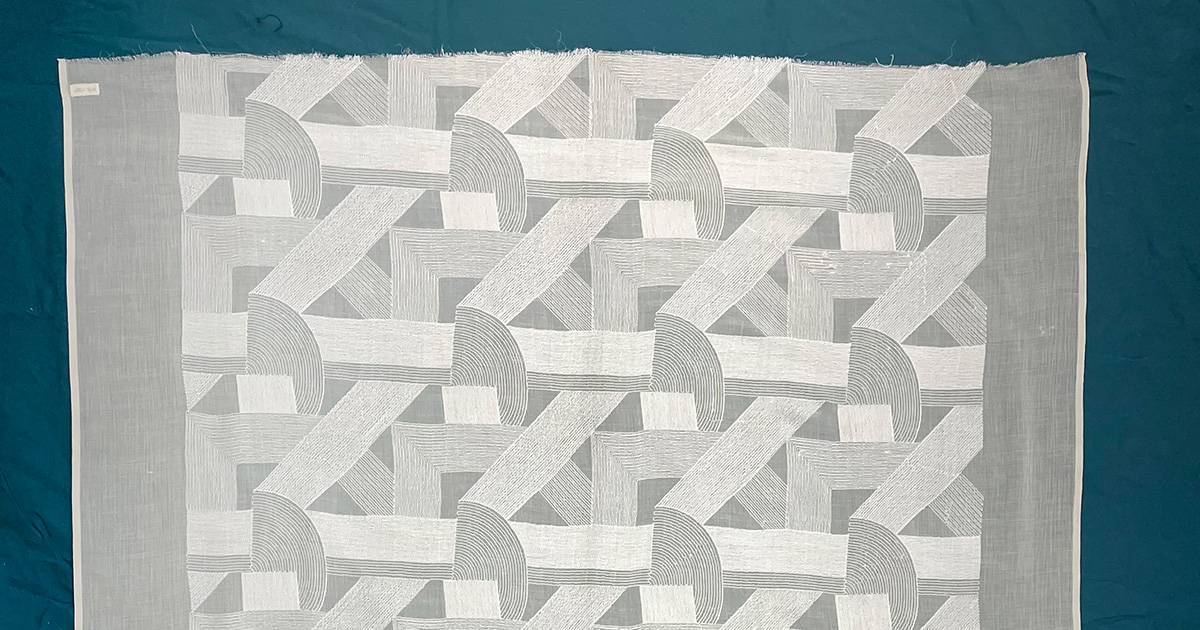 A light-colored fabric with a geometric pattern including rectangles & semicircles. 