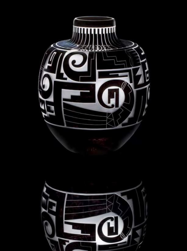 The vessel is black with white decoration. A series of geometric shapes in the form of squares, rectangles, stair steps, and what looks like the curling end of reptile tails encircle the vase.