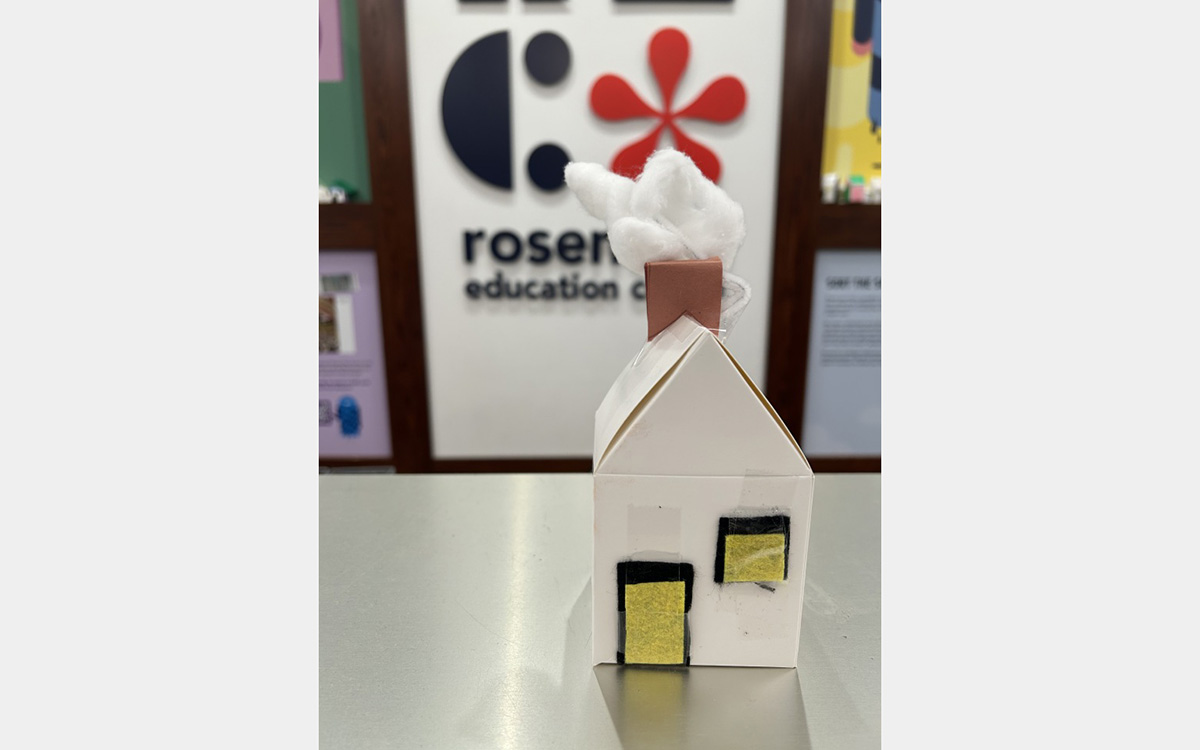 Small colorful model of a house on a tabletop with a "rosenthal education center" sign on wall in background.