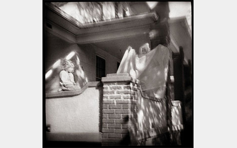 Nancy Rexroth's Playing Ghost, blurry, black and white photograph of two children on a brick banister railing outside of a home. The child on the right is wearing a sheet resembling a ghostly figure