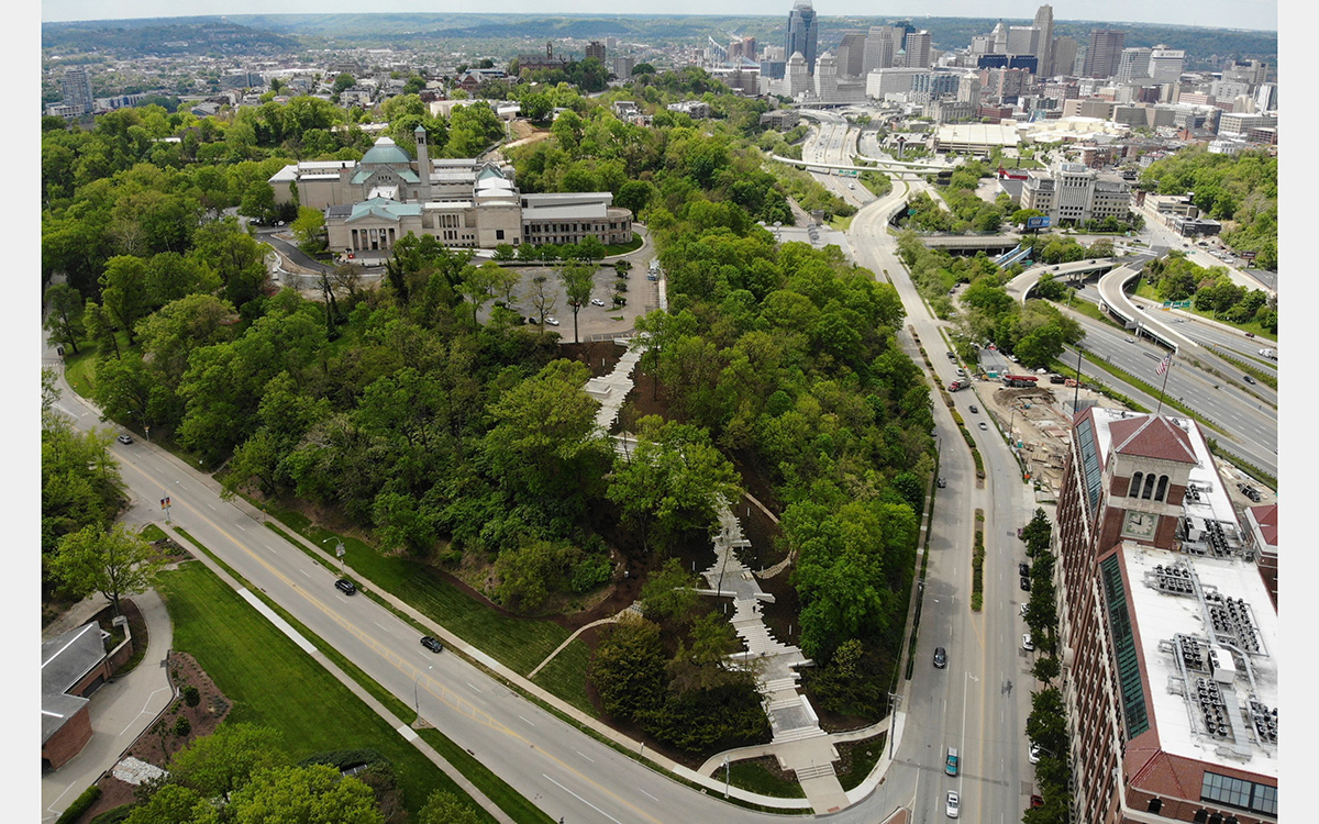 Green hill with staircase leading to a large building. In the background is a city with skyscrapers
