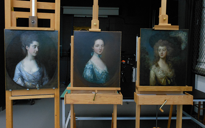 Three portraits of white women sit on wooden easels in the conservation lab.