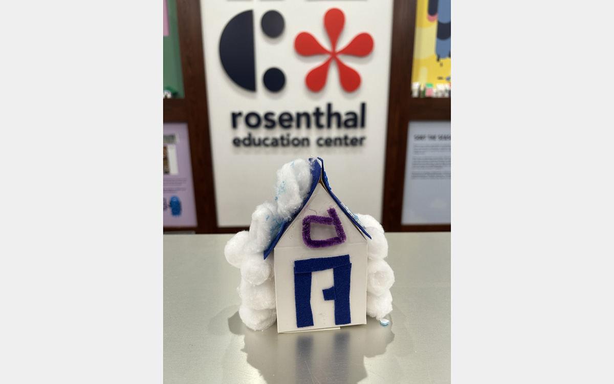Small colorful model of a house on a tabletop with a "rosenthal education center" sign on wall in background.