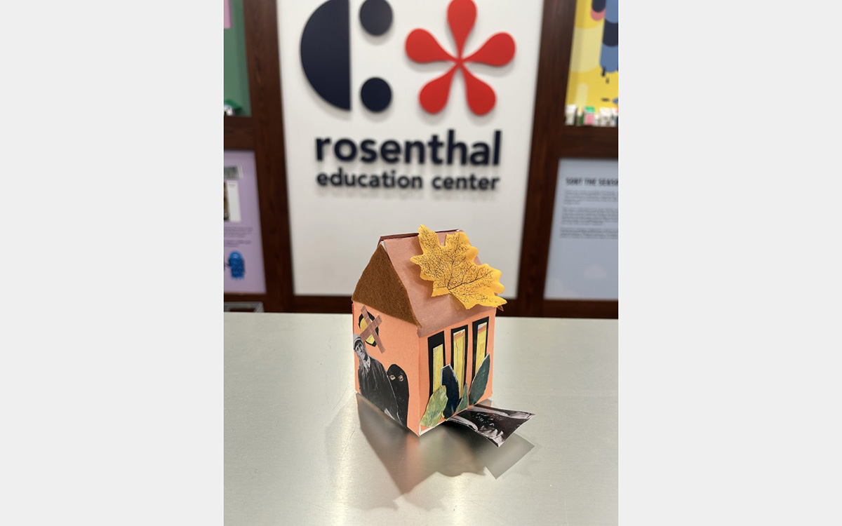 Small colorful model of a house on a tabletop with a "rosenthal education center" sign on wall in background.