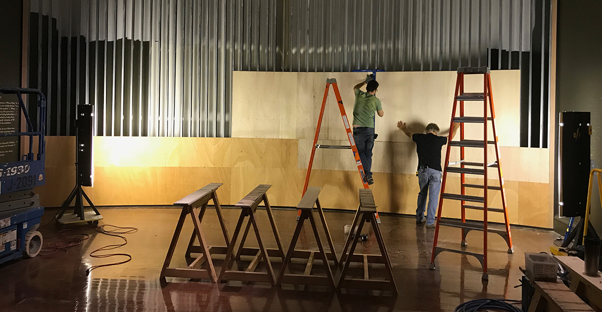 Two white men attach wood panels to a steel frame.