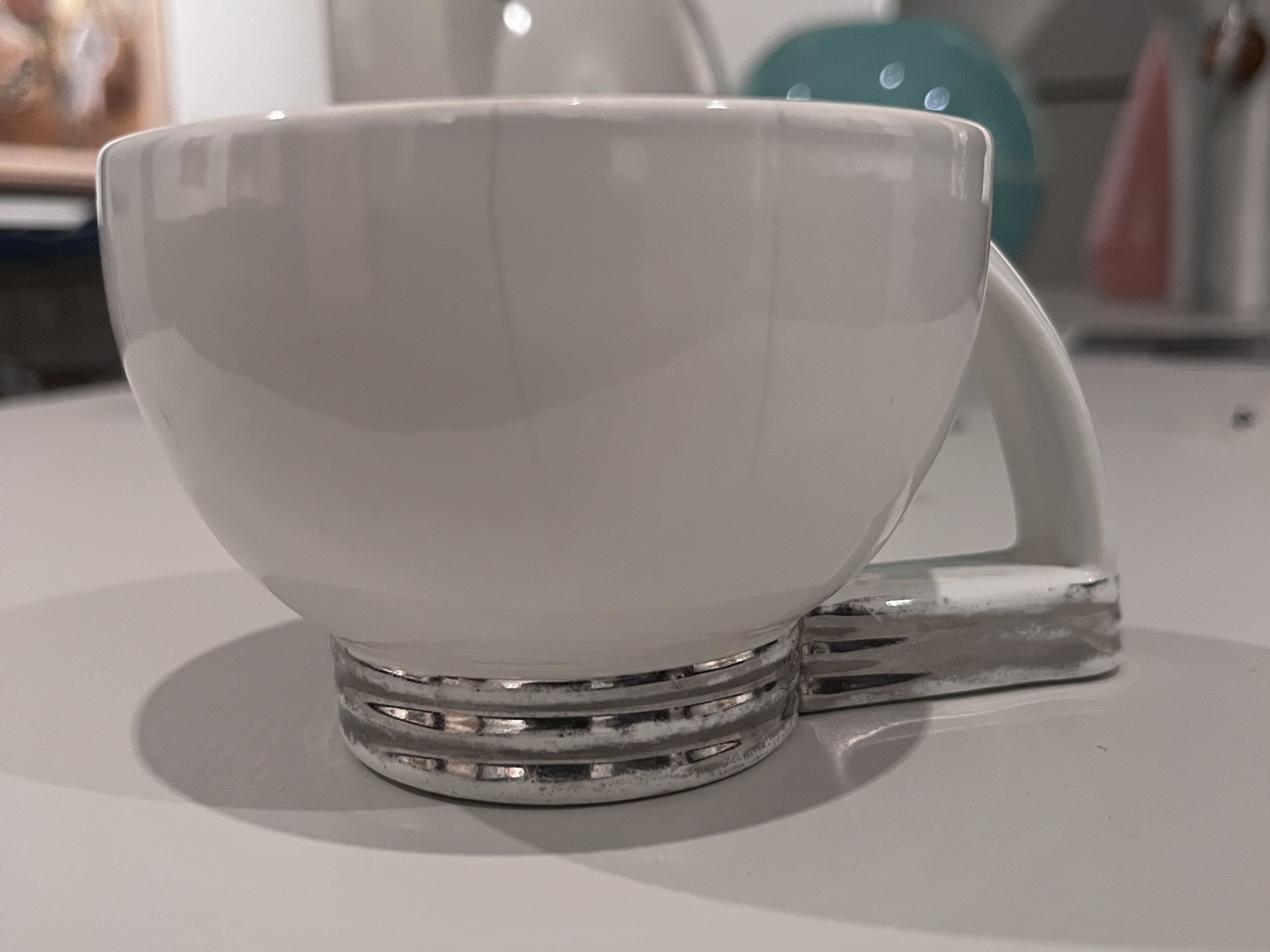 White ceramic teapot with chrome-colored ribbed base and angular handle