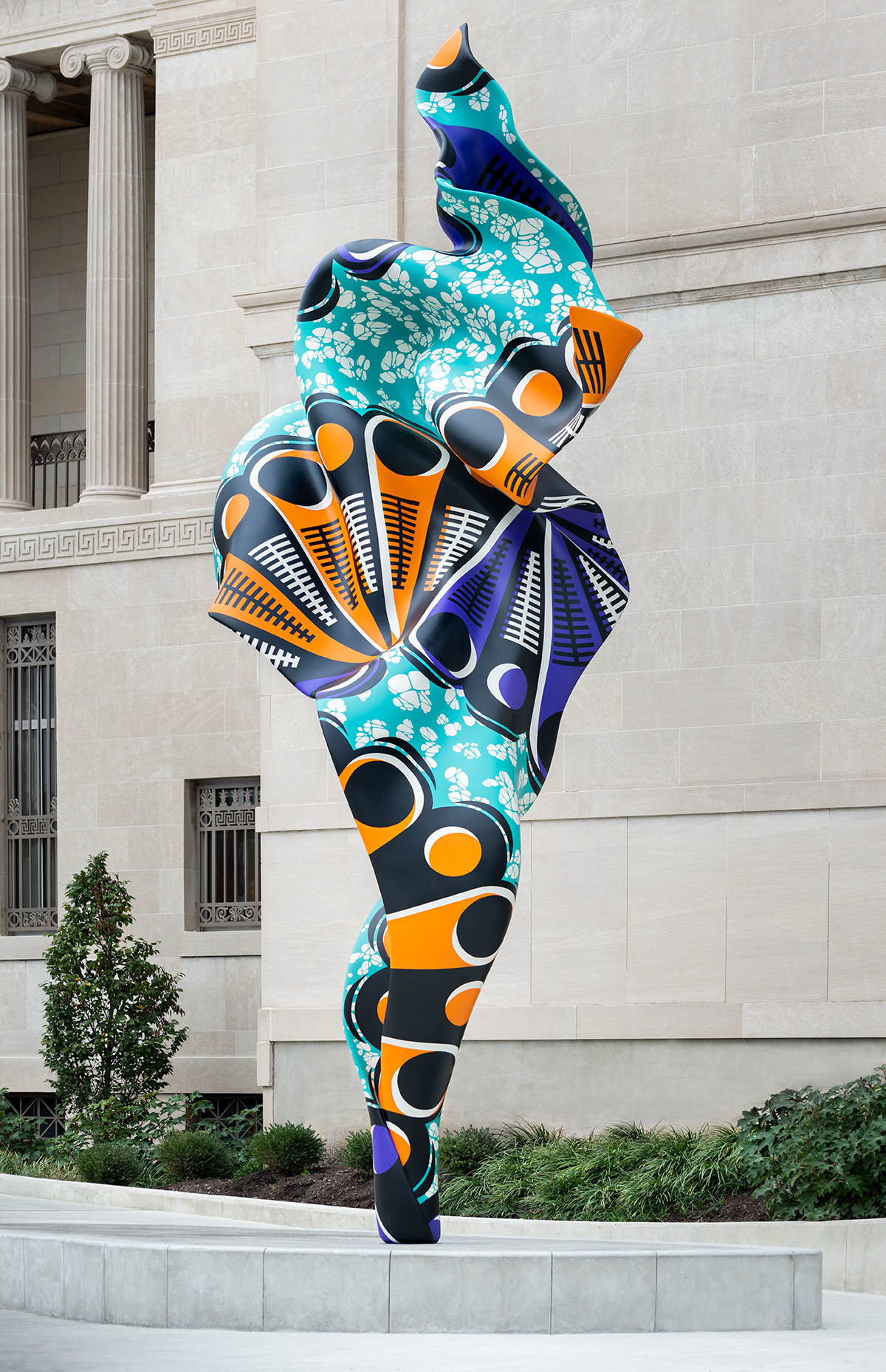 A tall, twisting sculpture with orange and purple shapes on a light blue background