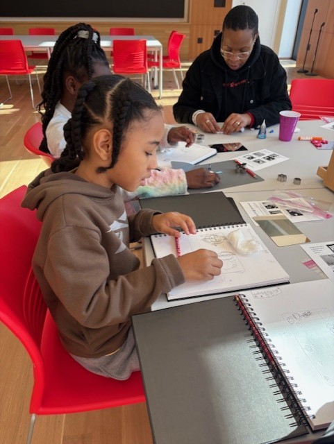 Two girls and one woman sit a table working on art projects.