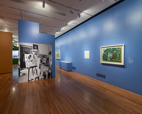 An installation shot featuring a black and white photo on a small blue wall and a painting on another blue wall