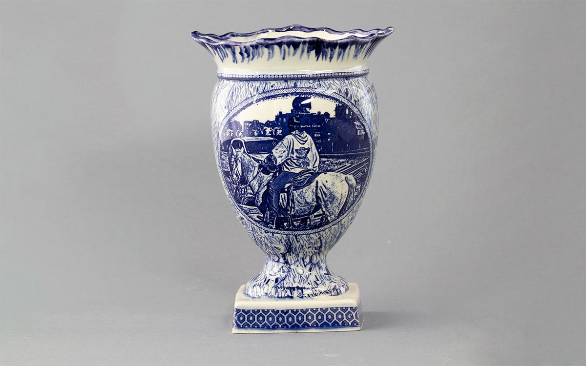 A large vase with a blue transfer of a person riding horseback with their back to the viewer.