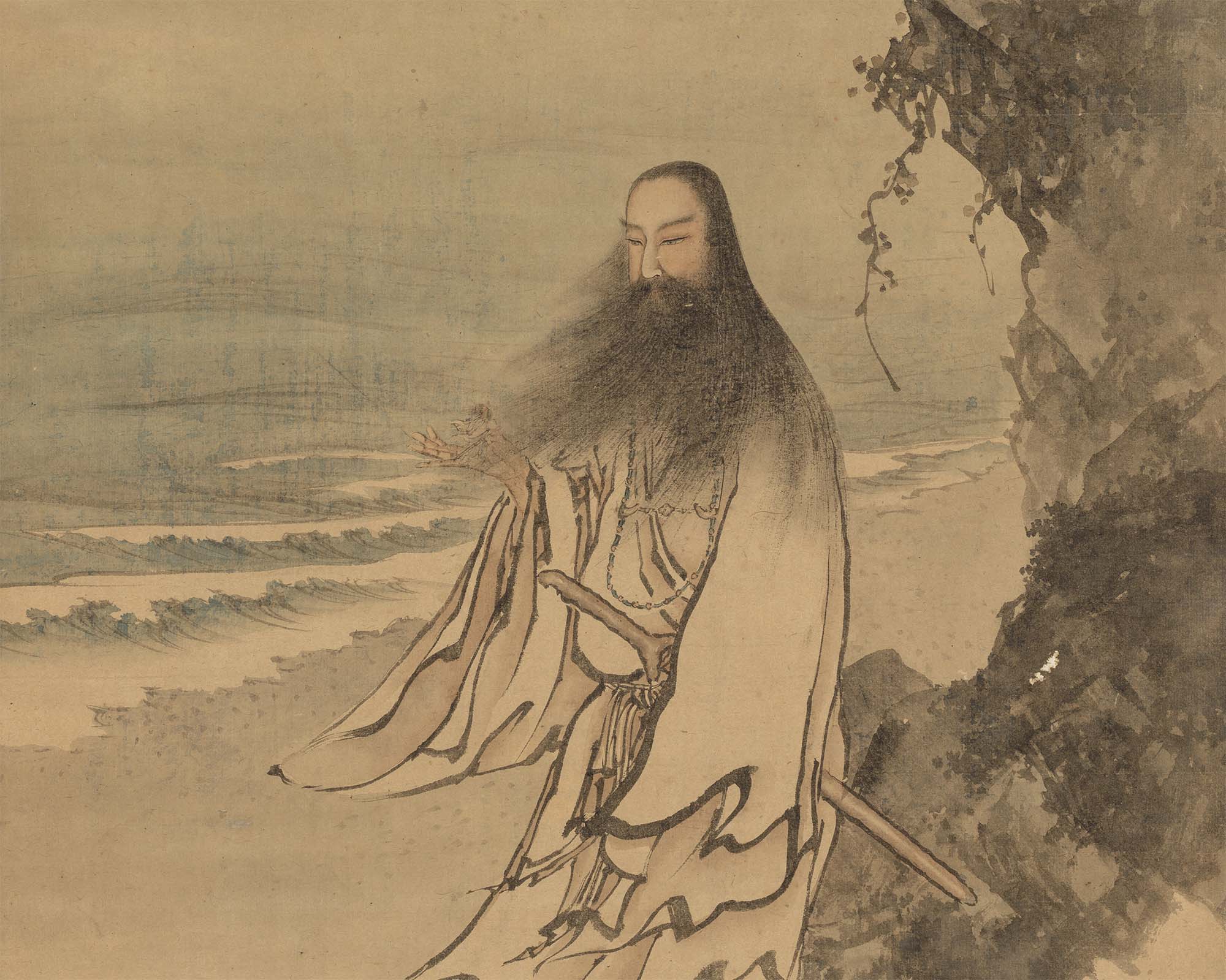 A man with long hair and beard in a cloak by the sea