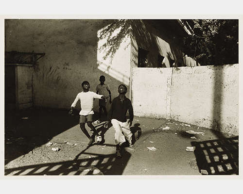 Three kids look up to the sky in a couryard in this black and white photo