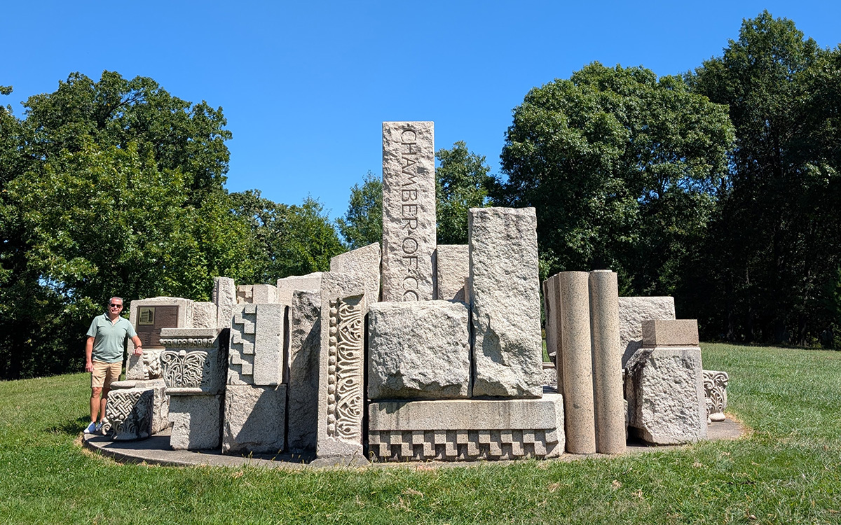 Man standing next to carved stones piled in a park-like setting.
