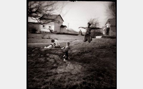 Nancy Rexroth's Boys Flying, a blurry black and white photograph of boys playing in a field. One boy leaps into the air with his arms outstretched to the sides like wings