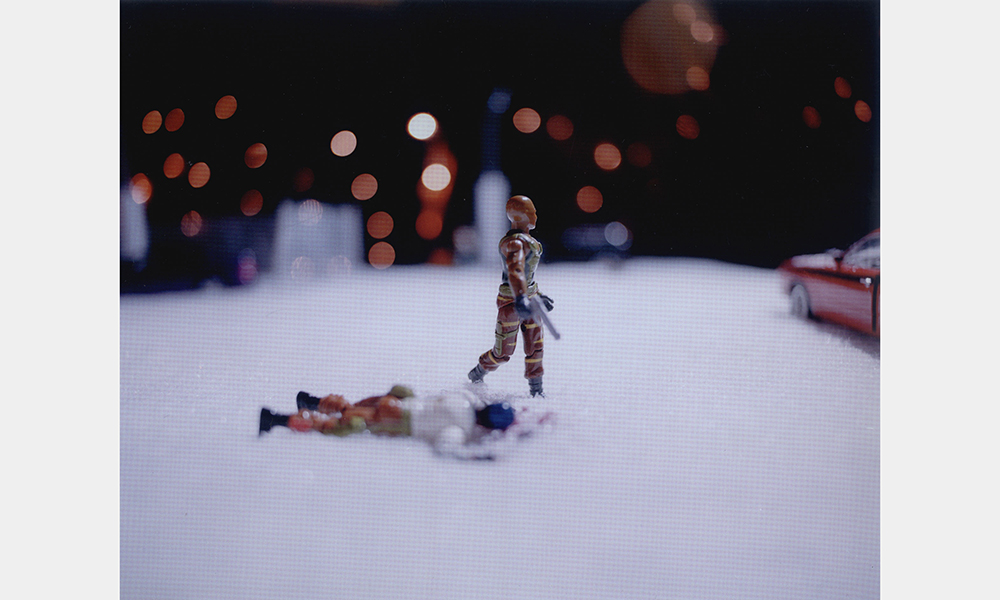 Hank Willis Thomas and  Kambui Olujimi's Winter in America, a still image of two small, toy figurines, one lies face down in snow, the other walks past carrying a silver handgun in its right hand