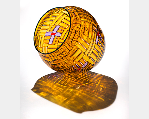 A clear yellow glass vessel that looks like a woven basket with white cross details with red centers