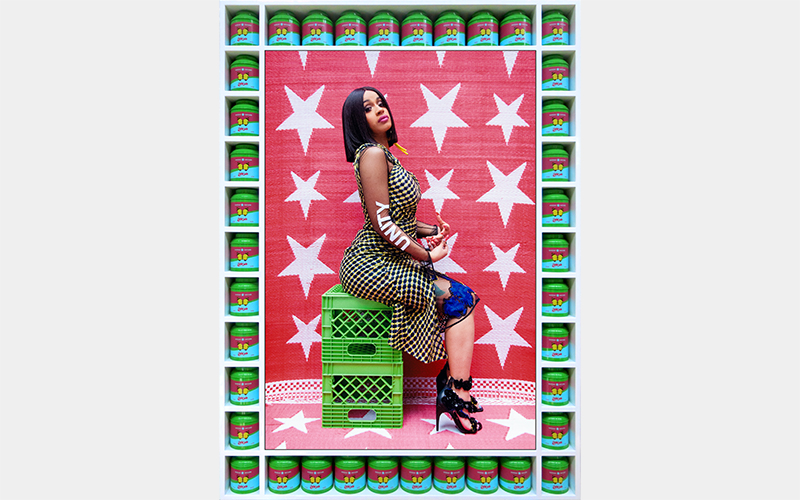 Cardi B sits on two green milk crates and looks at the camera. The word "unity" is spelled out on her arm.