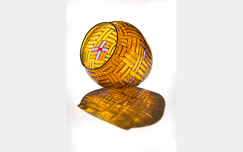 A clear yellow glass vessel that looks like a woven basket with white cross details with red centers