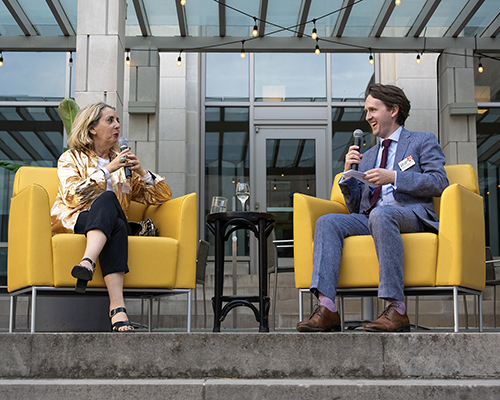 Two white people talk to each other in yellow chairs outdoors