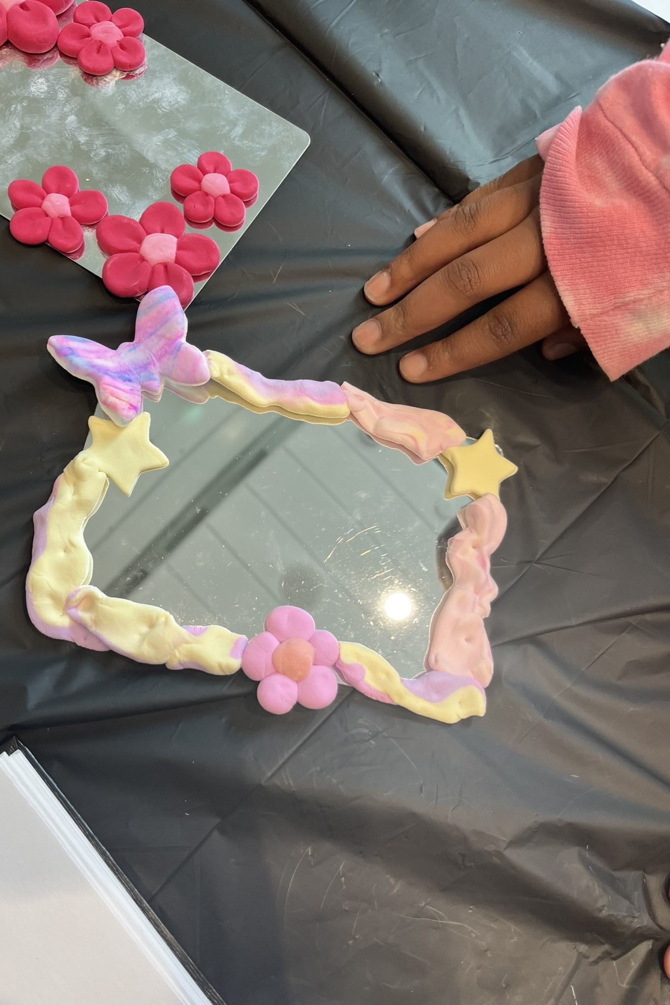 View from above of a child's hand with two artworks with handmade decorative frames mounted onto small mirrors.