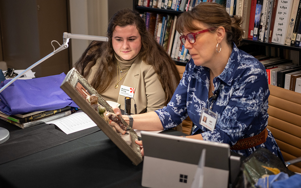 A curator and curatorial assistant look at an artwork under a light