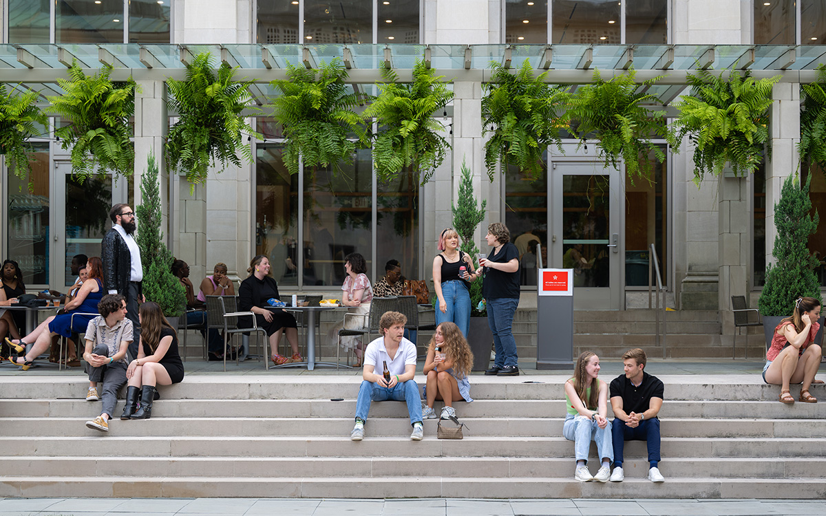 The courtyard outside of the museum's Terrace Cafe. Clusters of people sit and stand on steps -- the majority are groups of two. All of the duos are made up of people engaging with each other.