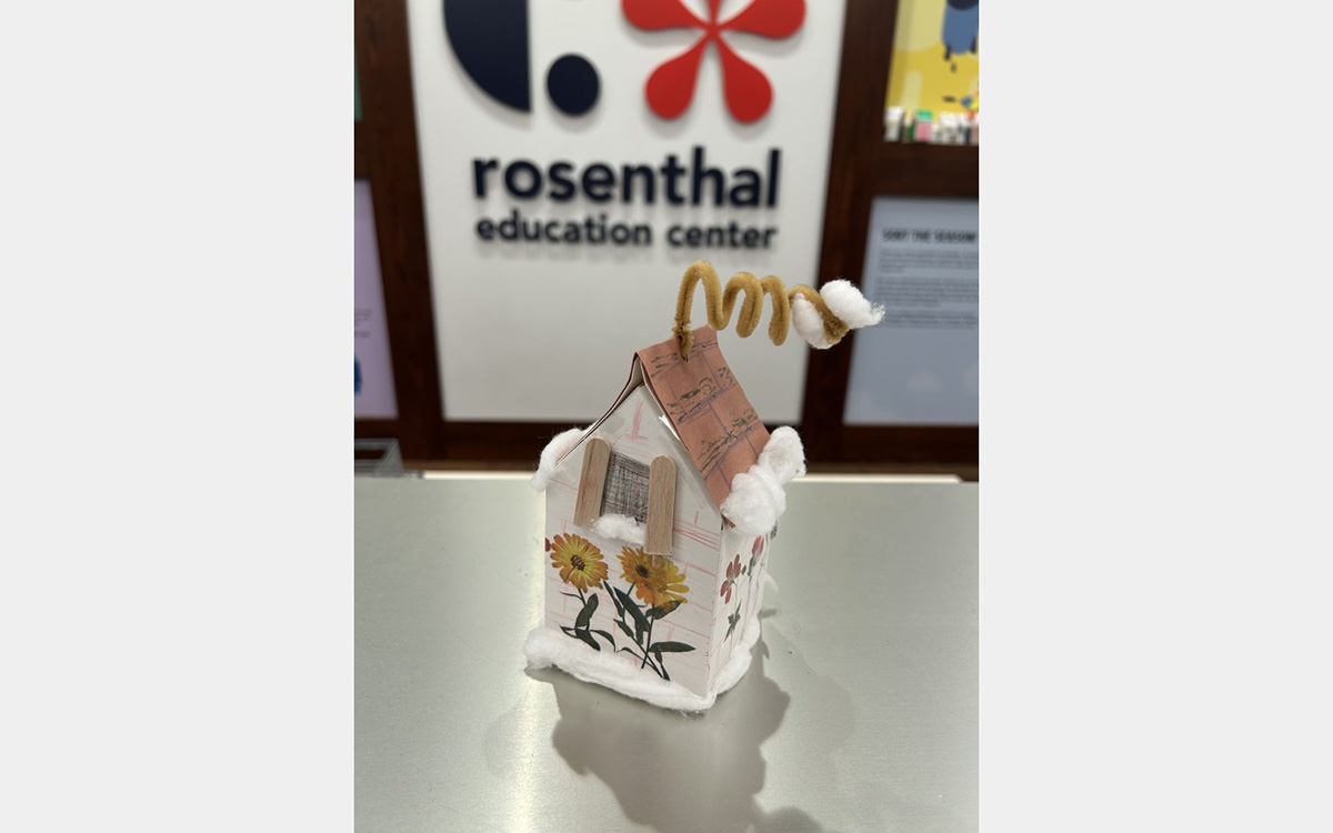 Small colorful model of a house on a tabletop with a "rosenthal education center" sign on wall in background.