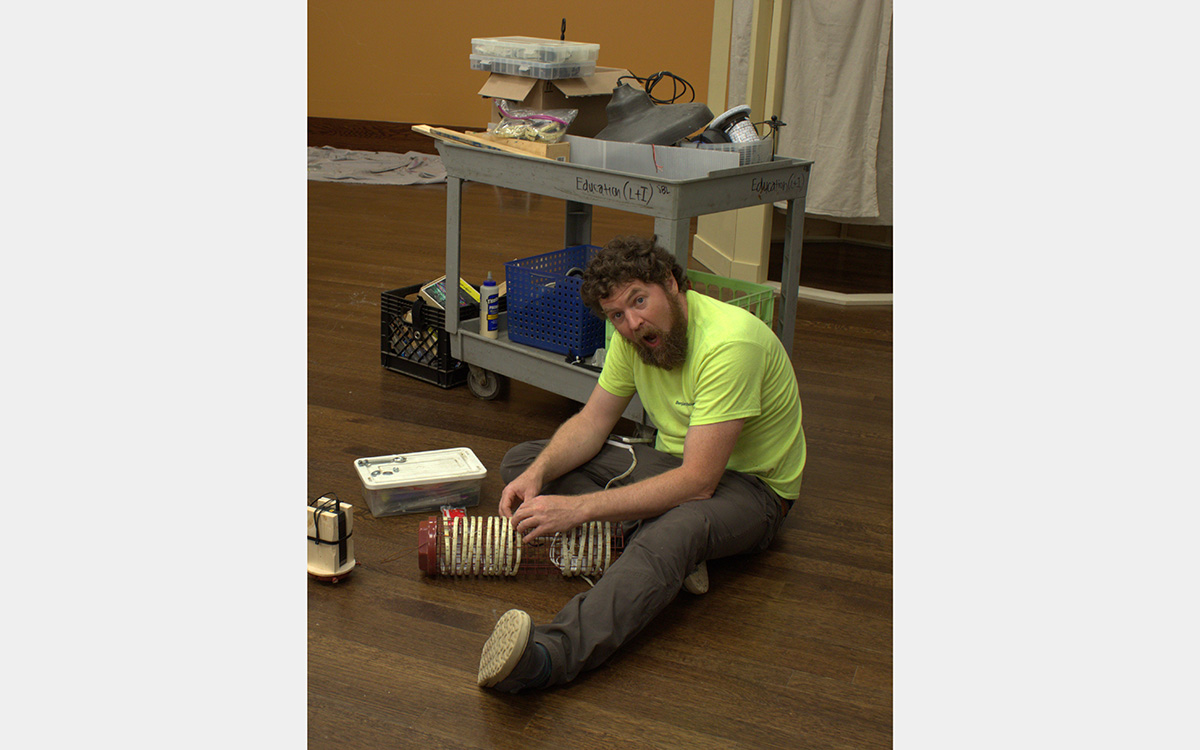 A man sits on a floor in front of a cart while wiring a light 