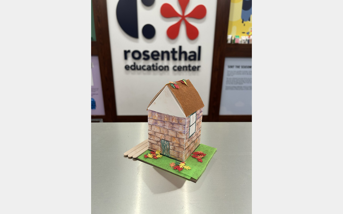 Small colorful model of a house on a tabletop with a "rosenthal education center" sign on wall in background.