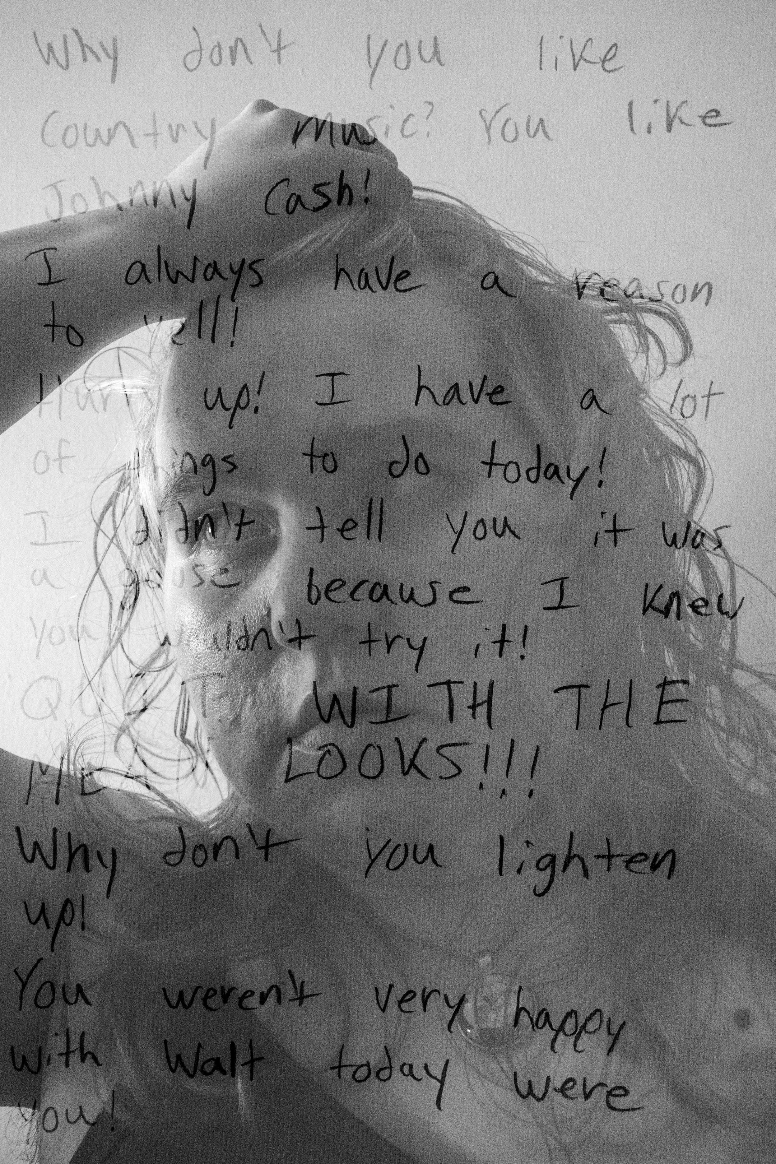 A black and white photo of a light-skinned person running their hand through their curly textured hair, with a distressed expression. Hand-written degrading words and phrases are superimposed over the photo.