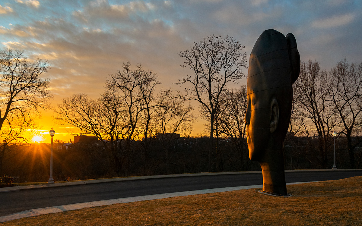 Sculpture of a girl's head looking out toward a sunset