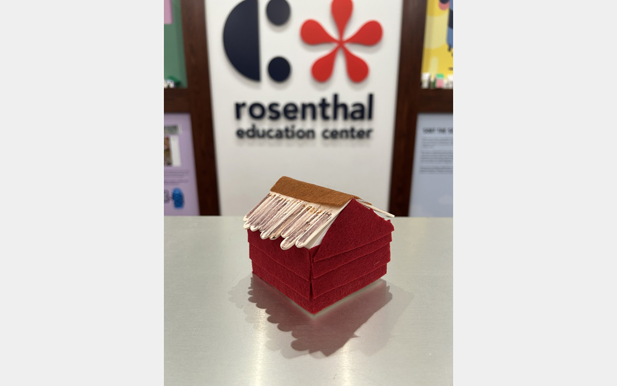 Small colorful model of a house on a tabletop with a "rosenthal education center" sign on wall in background.