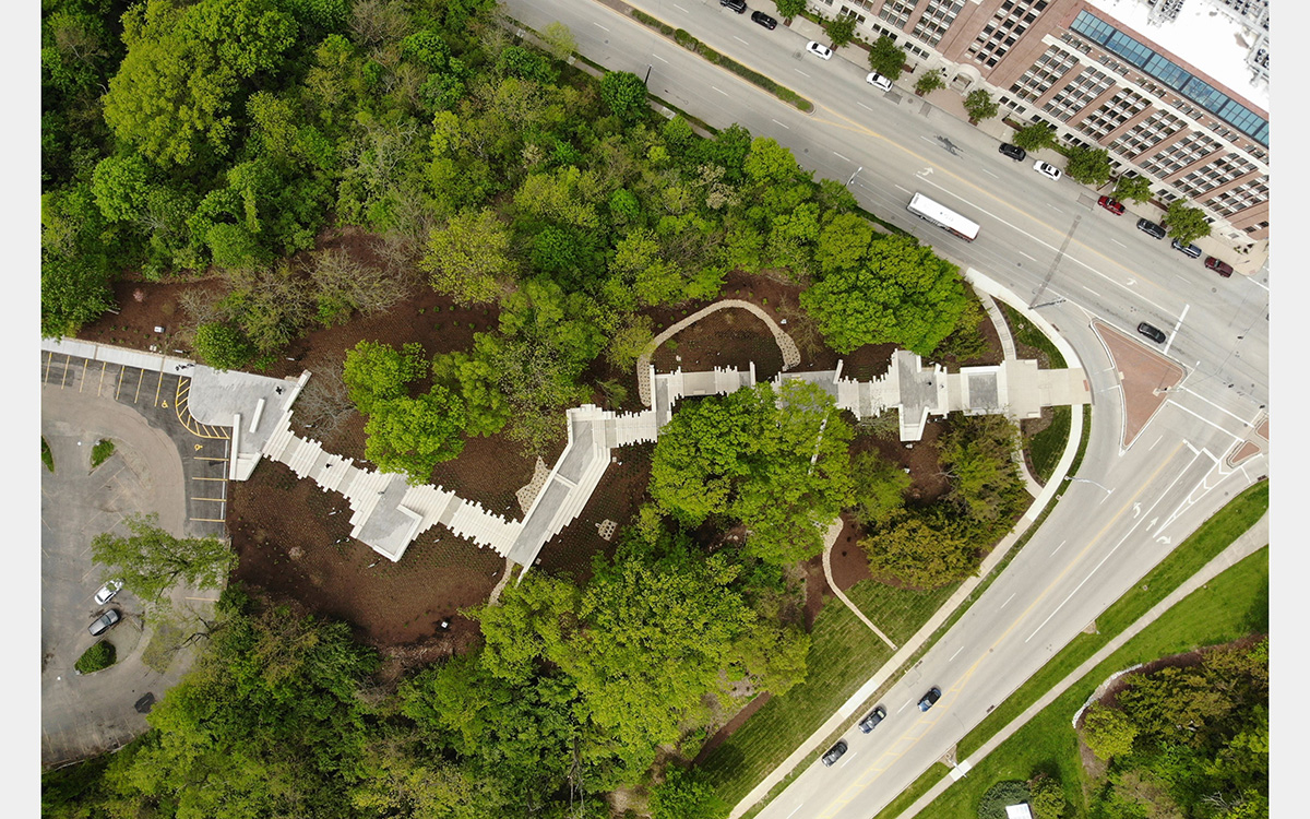 Aerial view of staircase zigzagging up a tree covered hill above a street intersection.