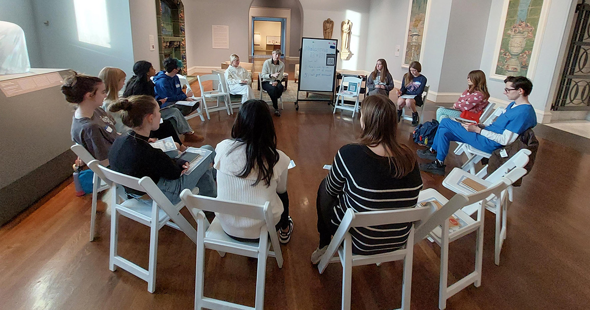 A group of young people sit in a circle in the museum.