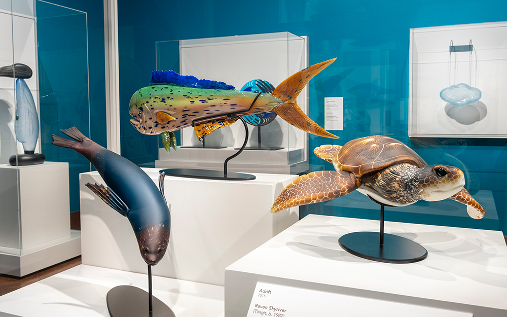 A brown and black seal, a green and brown fish with dark spots, and a light brown turtle made of glass mounted in a case.