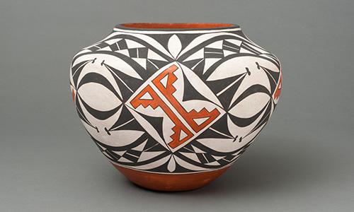 A painted ceramic vessel covered with sharp, black shapes and a geometric, orange design in the center.