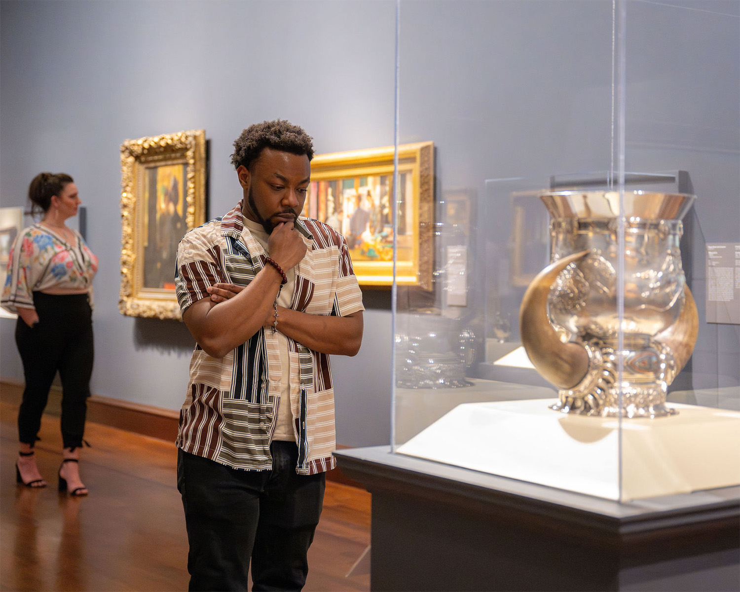 A Black man looks at a large silver pitcher in a glass case