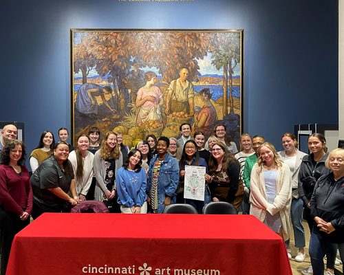 A large group of people pose in front of a large artwork