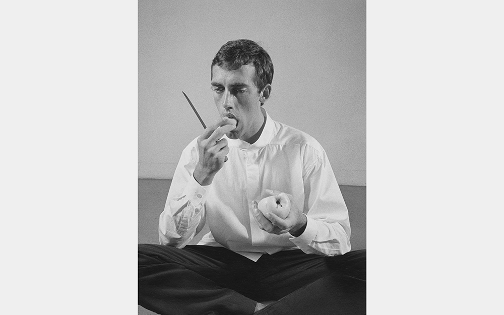 A black and white photo of a man holding a knife and putting a slice of apple in his mouth.