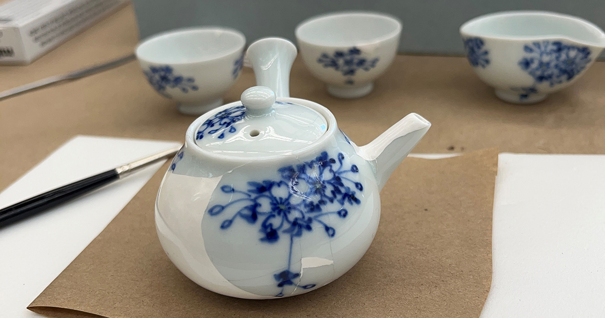A small white teapot with blue floral decoration