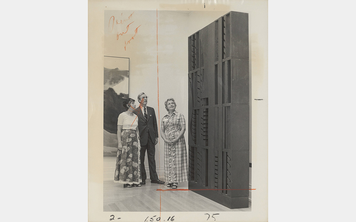 Black and white photo featuring three people looking at a box-like sculpture