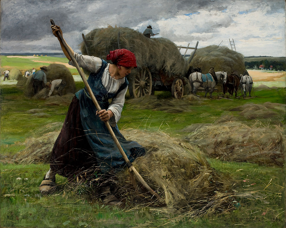 A woman with a red bandanna rakes hay