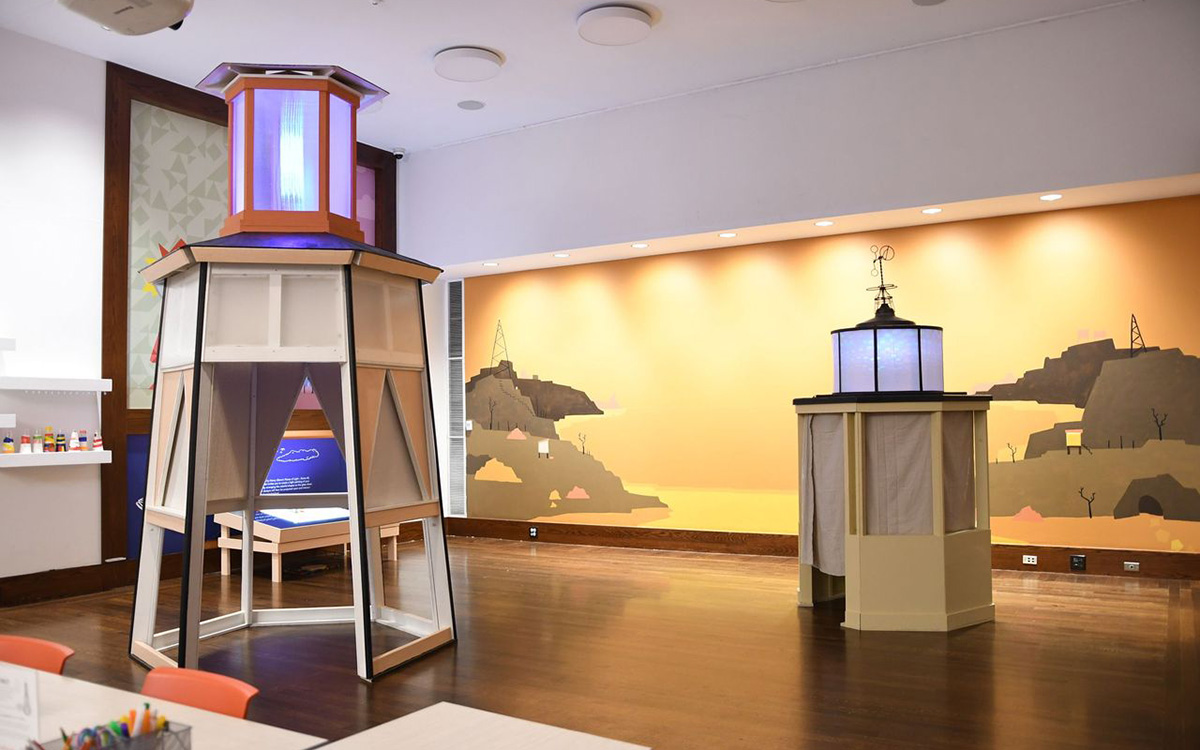 Two wooden tower-like structures inside a large room with a brightly background of a stylized harbor scene.
