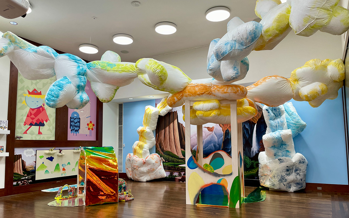 An installation featuring fluffy blue and yellow clouds descending from the ceiling and a mural of a waterfall